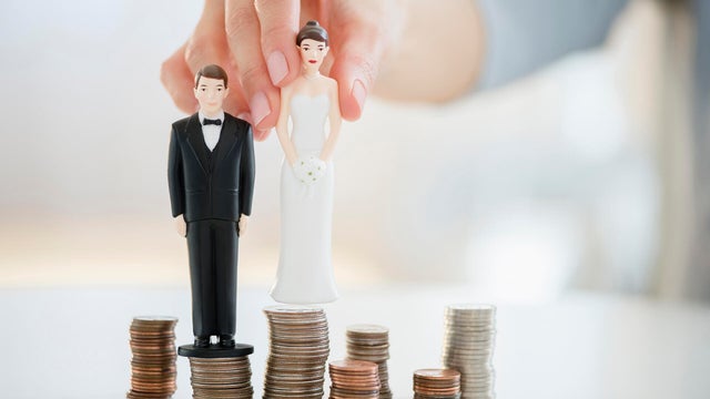 Mixed race woman balancing bride and groom statues on coin stacks 